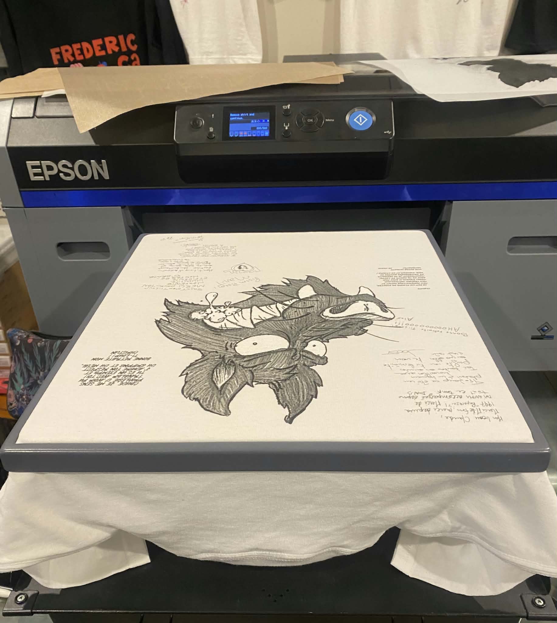 Notre imprimante textile Epson SureColor : un chandail blanc tendu sur le plateau, un dessin au trait en cours d'impression directement dans le coton.